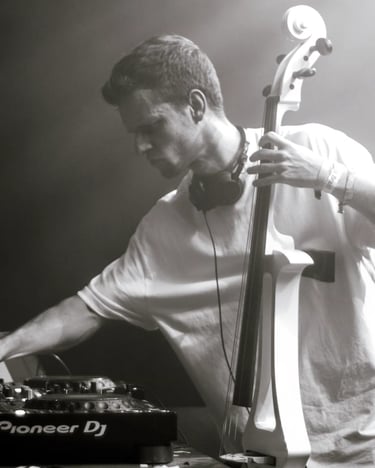 A male DJ performing a live electronic music set while playing a modern white electric cello.