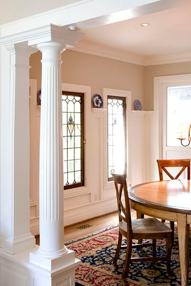 Elegant dining room featuring white fluted columns and vintage stained glass windows.