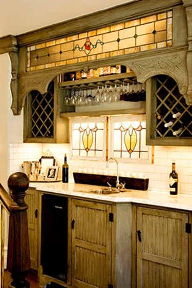 Rustic home wet bar with stained glass accents, custom grey cabinets, and a wine glass rack.