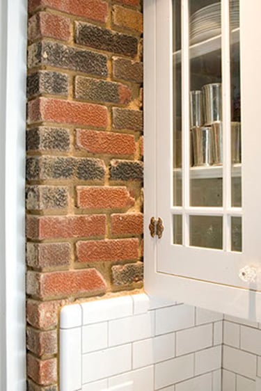 Rustic red brick wall feature next to white kitchen cabinets and subway tile backsplash.