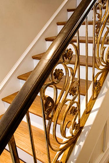 Elegant oak wood staircase featuring custom gold ornate wrought iron floral balusters and handrail.