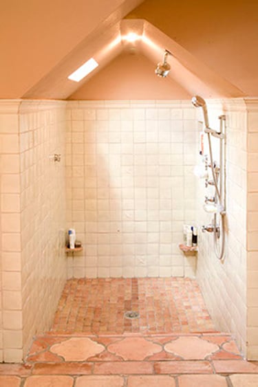 Rustic walk-in shower with terracotta floor tiles and white wall tiling under a sloped attic ceiling.