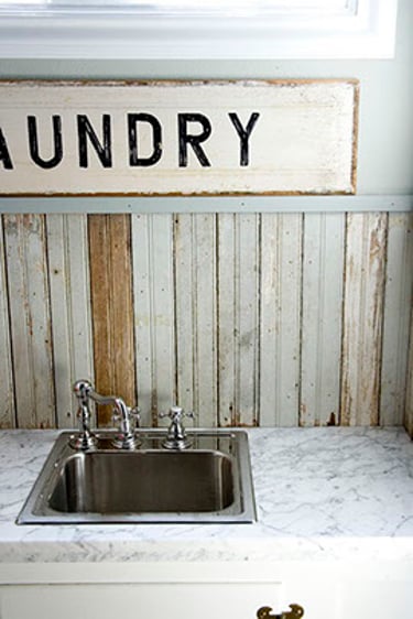 Rustic laundry room utility sink with a marble countertop and vintage wooden laundry sign.