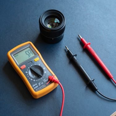 A professional flat-lay photograph of electrical testing tools, a multimeter, and insulated screwdrivers on a dark blue technical surface, clean and organized composition.