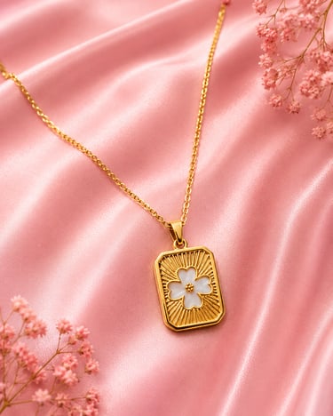 Gold clover necklace with white flower pendant on elegant pink silk fabric with baby's breath flowers.