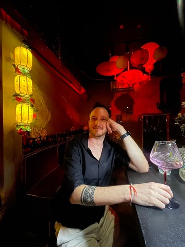 Unicris enjoying a cocktail at a dimly lit bar with red and yellow Chinese lanterns.