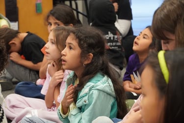 Diverse elementary students sitting on the floor listening attentively during a primary school classroom lesson.