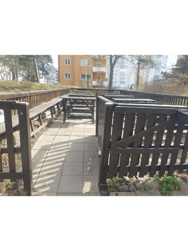 Outdoor wooden picnic tables inside a fenced patio area with a stone walkway in a residential courtyard.