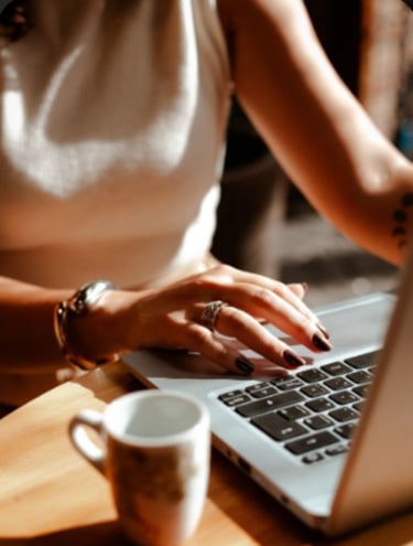 Una mujer escribe en el teclado de una computadora portátil en una mesa de café iluminada por el sol