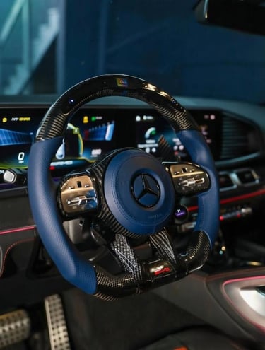 Custom blue and carbon fiber Mercedes AMG steering wheel inside a luxury car interior.