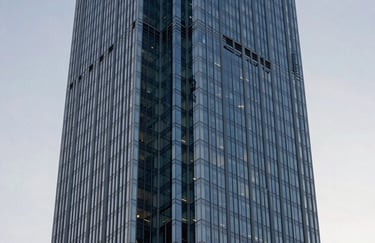 A sharp architectural detail photograph of a modern skyscraper in a North American city. The focus is on the geometric patterns of the glass and steel blue frames against a soft gray sky.