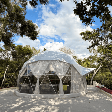 A luxurious white geodesic dome, Venamarte Glamping, nestled in the Mayan Jungle under a blue sky.