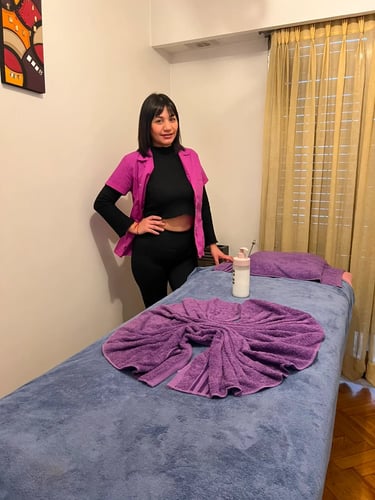 Masajista profesional Mica con ambo fucsia al lado de la camilla de masajes en su consultorio de Caballito.
