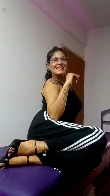 Tama masajes sensuales Palermo, sentada con outfit deportivo y anteojos en su espacio de relax.