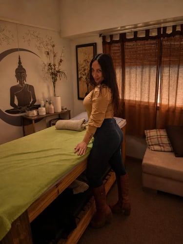 Gabinete privado de Pili masajes sensuales en Flores, posando con remera amarilla junto a la camilla.