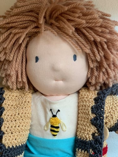Muñeco Waldorf con cabello de estambre castaño, con playera bordada con una abeja y sueter amarillo 