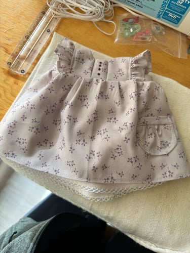 Vestido lila con flores para muñeca waldorf en el fondo una regla y material de costura