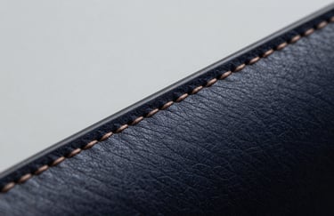 A macro shot focusing on the fine stitching of a Deep Midnight leather product against a Pure Mist background.