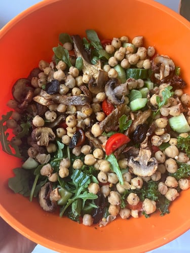 A healthy vegan chickpea salad with roasted mushrooms, arugula, and tomatoes in an orange bowl.