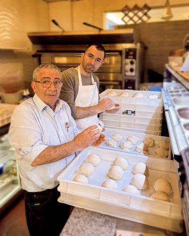 Two pizzaiolos, an older man and a younger man, prepare fresh pizza dough in a commercial kitchen, showcasing artisanal