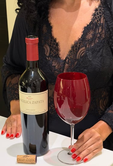 Iria, vestida com um vestido de renda preto, posa com uma garrafa de Angelica Zapata Malbec e uma gr