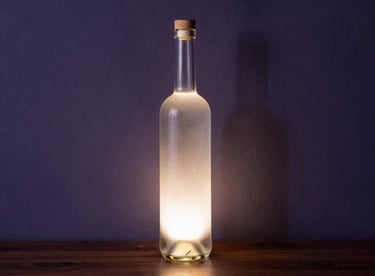 A unique Pisco bottle repurposed as a designer lamp, glowing softly against a dark purple charcoal wall in a South American / Peruvian home.