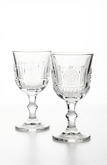 A set of two engraved Pisco glasses with intricate South American / Peruvian motifs, minimalist photography on a pure white background.