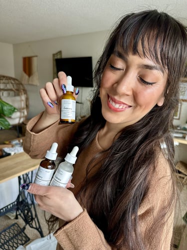 Ryanne holding three bottles of products by The Ordinary smiling with her eyes closed