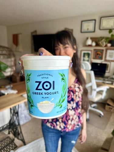 In-focus shot of a tub of yogurt being held by a girl out of focus behind it