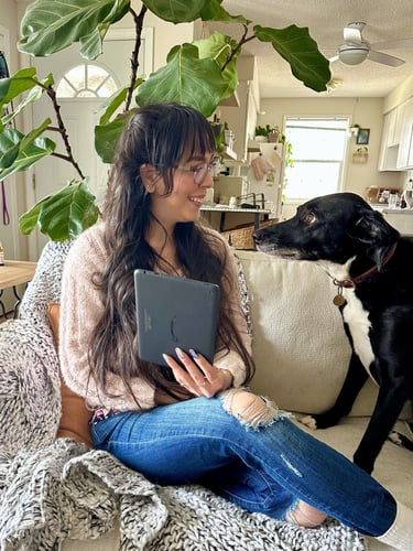 A girl holding a Kindle on a couch next to a black dog