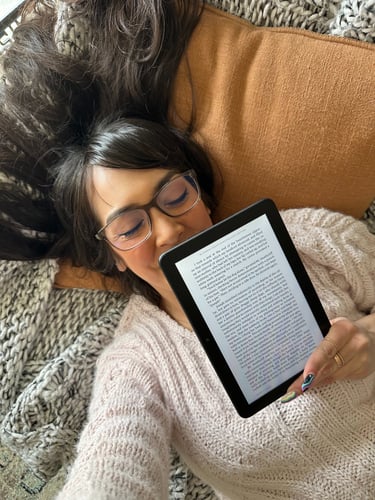 Overhead shot of a girl holding a kindle showing a page of a book with her eyes closed
