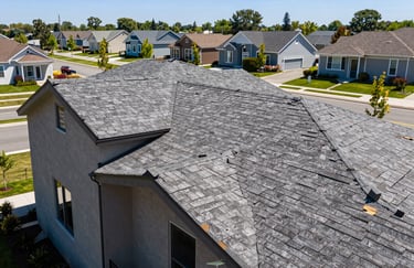 Professional photography of a completed roof restoration on a modern house with cedar shake accents. The house is situated in a clean, upscale US suburban neighborhood during a sunny day.