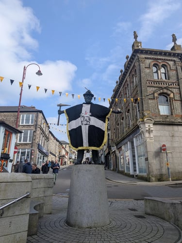 The bronze Tin Miner statue in Redruth, Cornwall wearing a large black and white Saint Piran's flag.