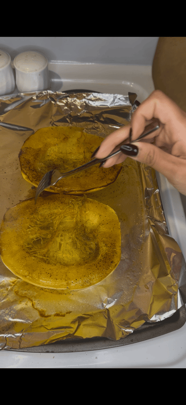 A person shreds roasted spaghetti squash with a fork on a foil-lined baking sheet.