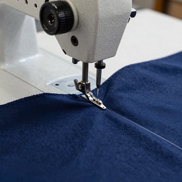 Close-up of industrial sewing machine needles working on high-quality navy blue cotton fabric in a professional Argentinian atelier, sharp focus on craftsmanship.