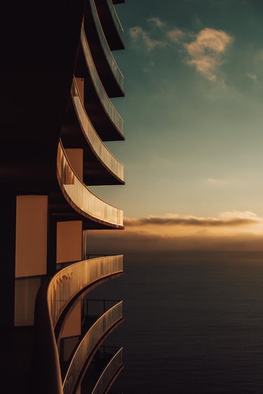Modern high-rise apartment balconies overlooking the ocean at sunset with golden hour lighting.