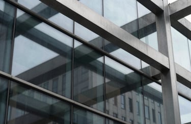 Close-up detail of a modern architectural facade featuring sleek glass panels and brushed steel beams, reflecting a charcoal and light gray palette.