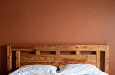 A close-up of a perfectly painted terracotta feature wall behind a stylish South American / Brazilian wooden headboard in a master suite. Soft, inviting morning light.