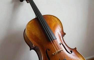 A close-up of a wooden cello resting against a soft mist white wall, focused on the strings and craftsmanship.