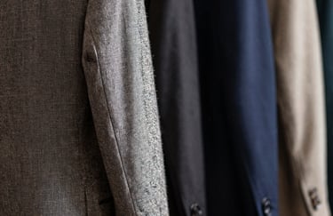 Close-up of high-quality fabrics and tailored suit jackets in a Brazilian design studio, soft shadows, textures of linen and wool, professional lighting.