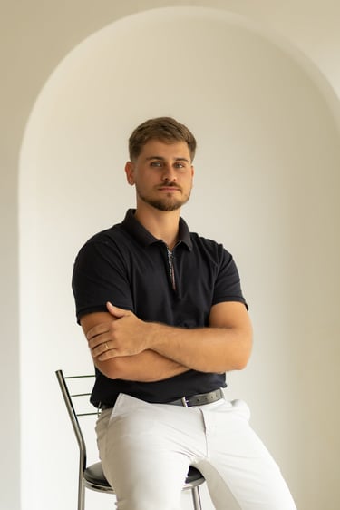 Homem profissional com os braços cruzados vestindo uma camisa polo preta e calças brancas