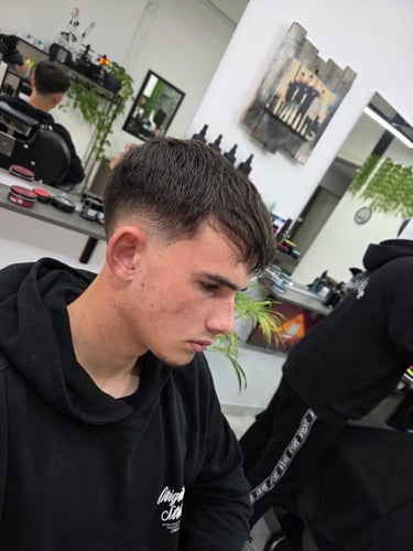 Young boy with a fresh skin fade haircut at a modern barbershop with blurred background.