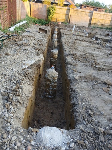 Concrete foundation piles installed in a deep trench at a residential construction site.
