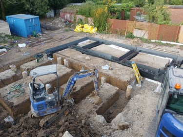 Aerial view of a construction site with a blue mini excavator digging foundation trenches for a new house.
