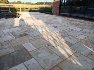 Modern garden patio featuring multi-tonal Indian sandstone paving slabs and a backyard pond.