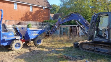 A blue mini excavator loading soil into a site dumper on a residential garden construction site.