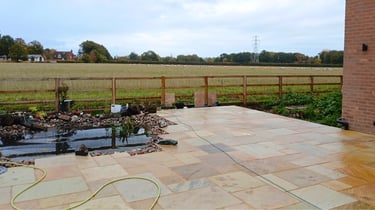 Sandstone patio with a garden pond overlooking a green field with sheep and a wooden fence.