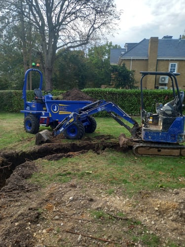 A blue micro excavator and tracked dumper digging a narrow trench for garden landscaping and groundworks.