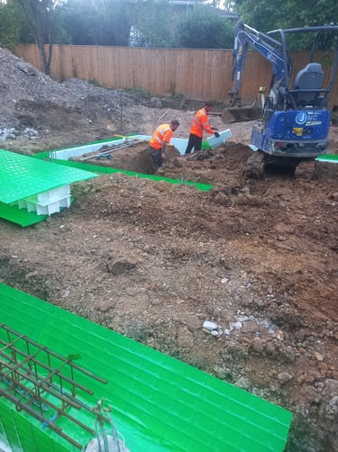 Construction workers installing green insulated concrete forms for building foundations with a mini excavator.