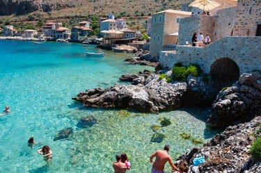 Tourists swimming in the turquoise waters of Limeni, a coastal village in Mani, Greece.